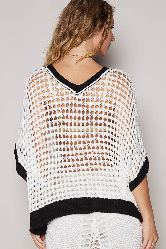 Woman wearing a white crochet top with black trim on a plain background