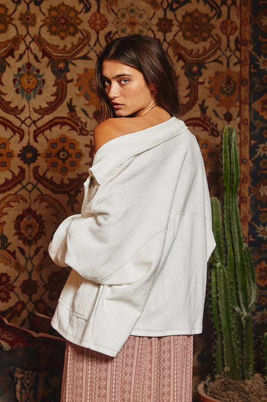 Woman wearing a light-colored off-shoulder top against a patterned wall with a cactus plant.