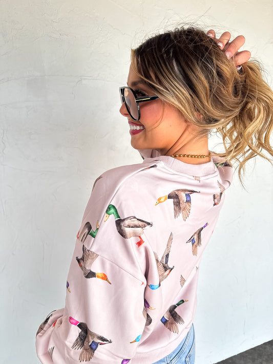 Woman wearing a pink hoodie with duck prints against a white wall