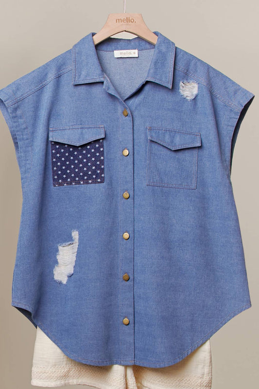 Blue sleeveless shirt with patchwork design on a hanger against a neutral background.