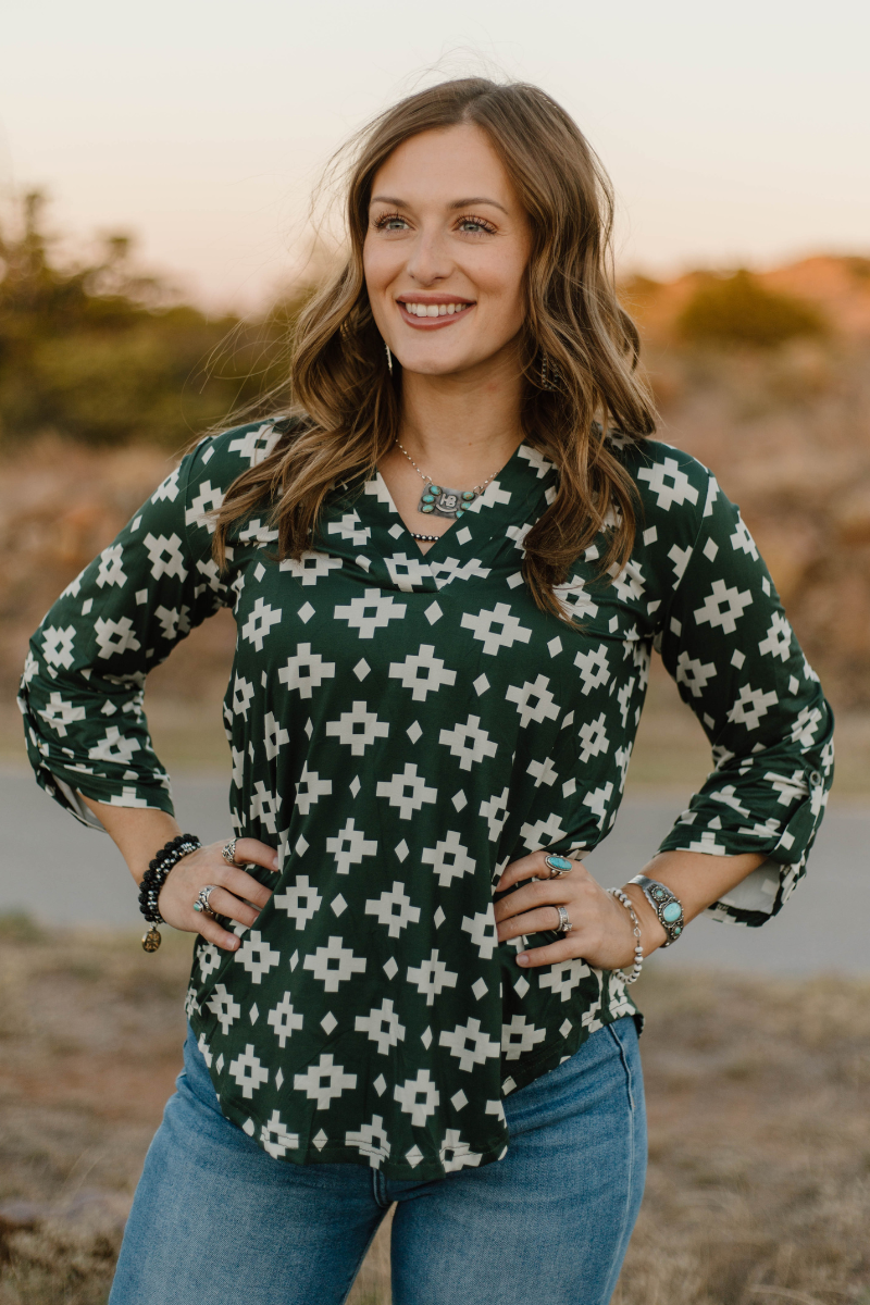 Woman wearing a green patterned blouse with blue jeans outdoors.