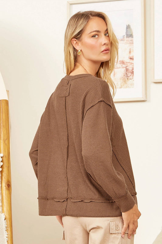 Woman wearing a brown textured sweater in a room with framed pictures on the wall.