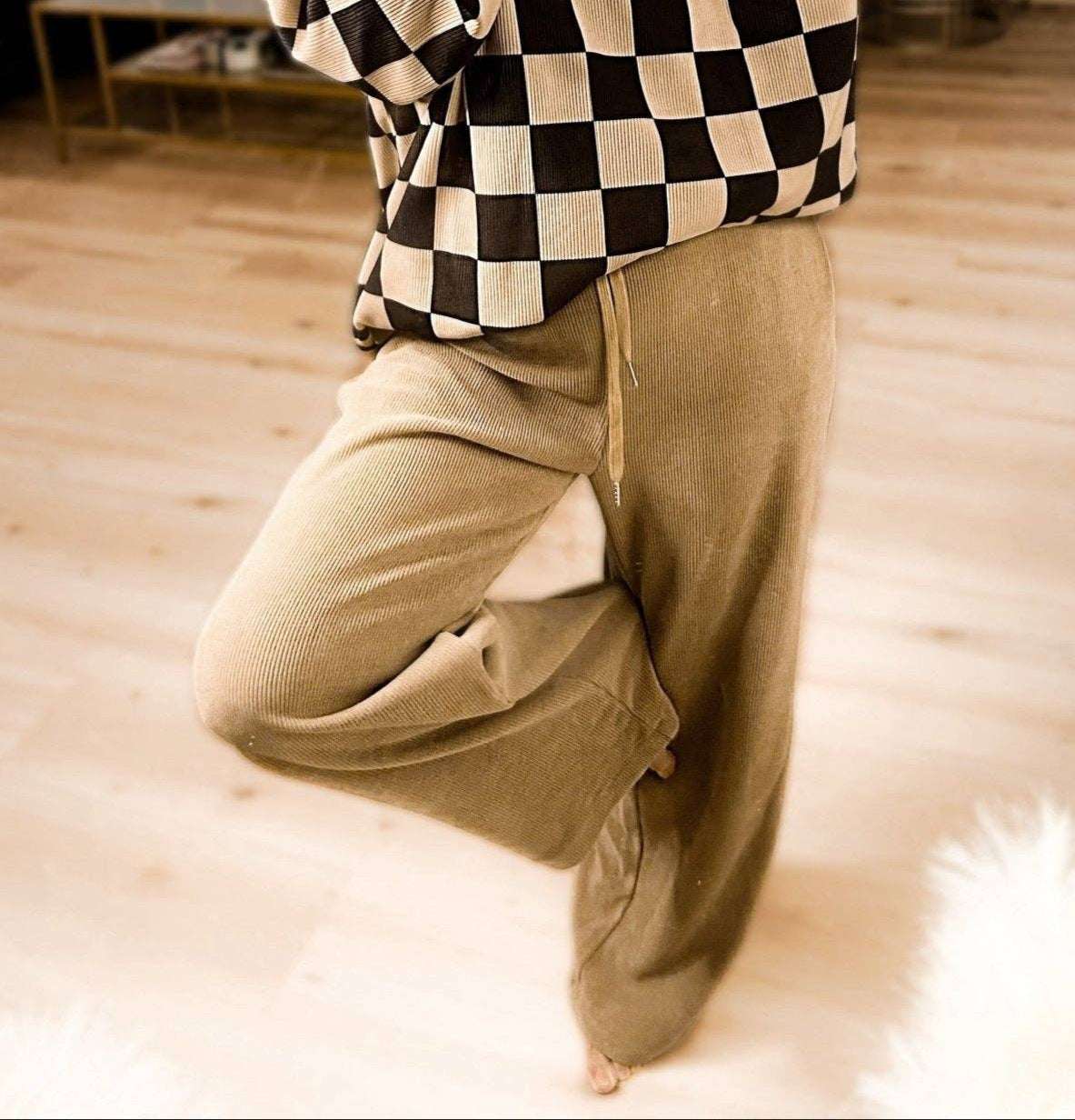 Person wearing a checkered shirt and beige pants on a wooden floor.