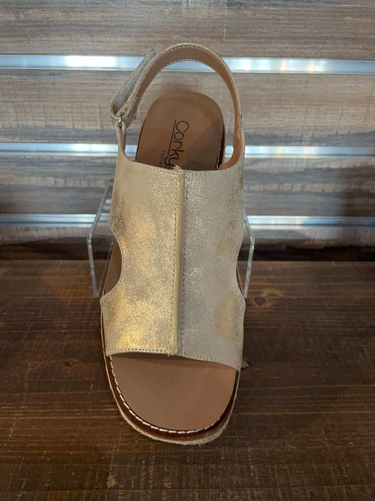Gold sandal with cork sole on a clear stand against a wooden background