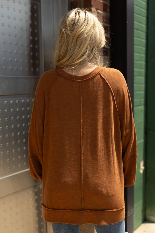 Person wearing a brown sweater standing in front of a textured wall.