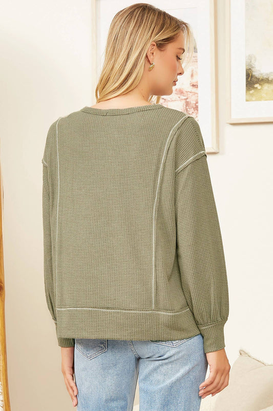 Woman wearing a green waffle knit sweater and blue jeans indoors.