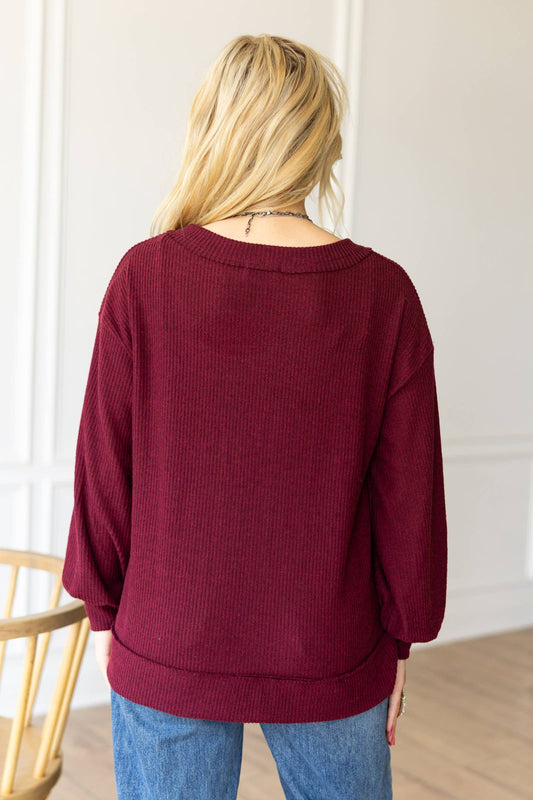 Person wearing a burgundy sweater and blue jeans in a minimal indoor setting