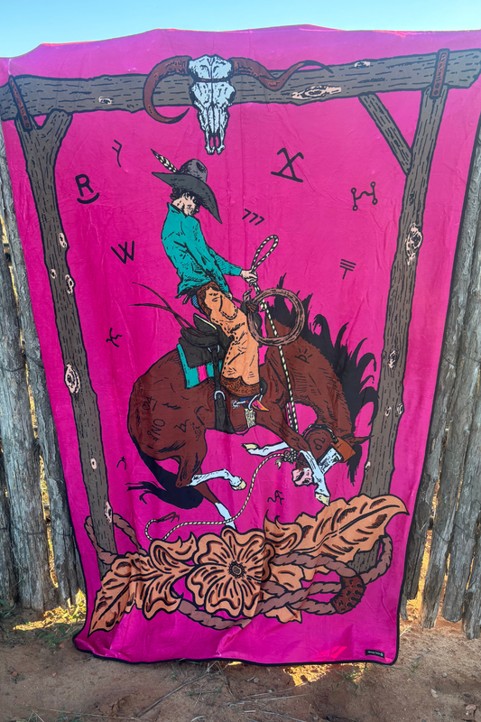 Pink blanket with a cowboy and horse design, featuring a wooden frame and skull.
