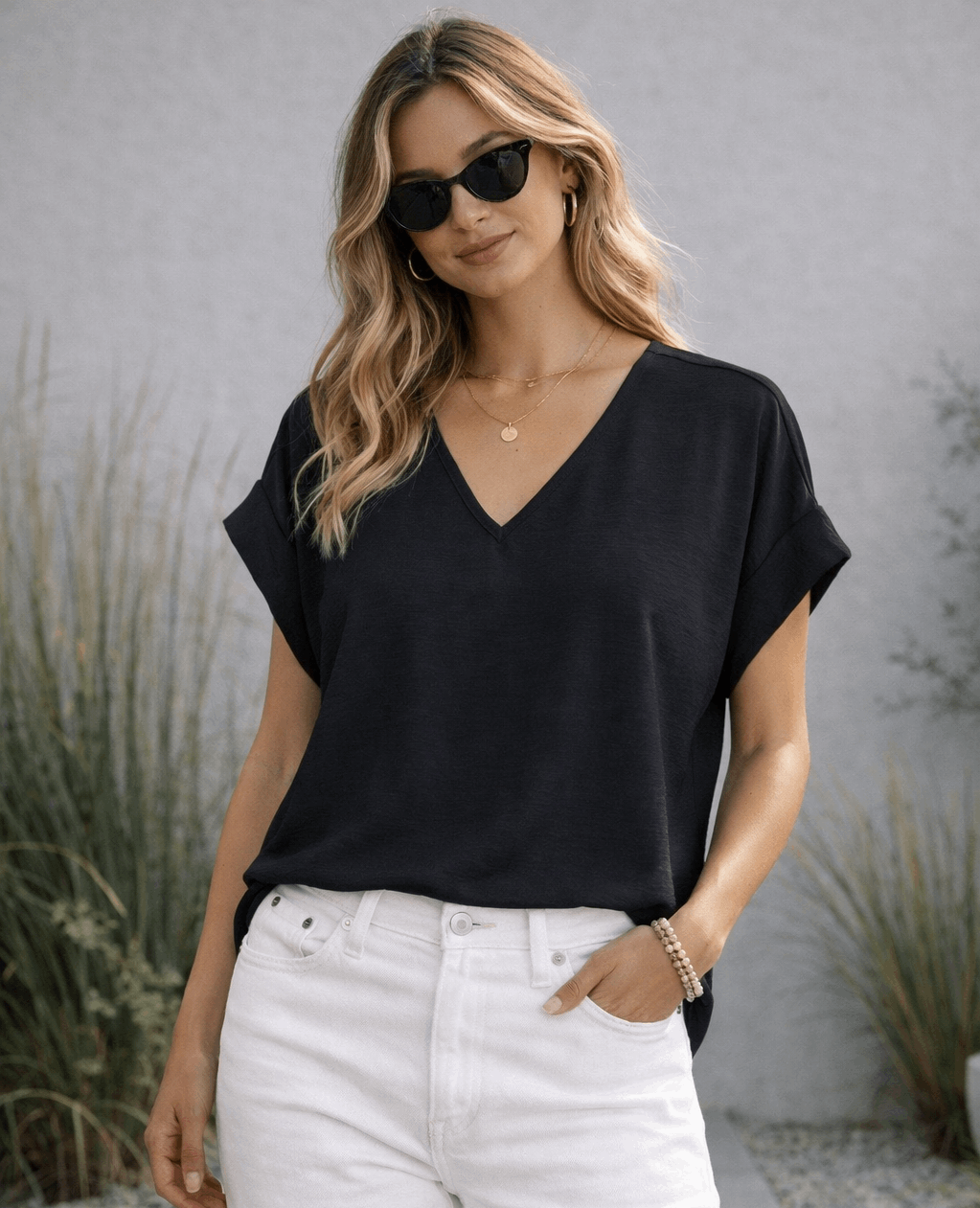 Woman wearing a black top and white pants with sunglasses outdoors.