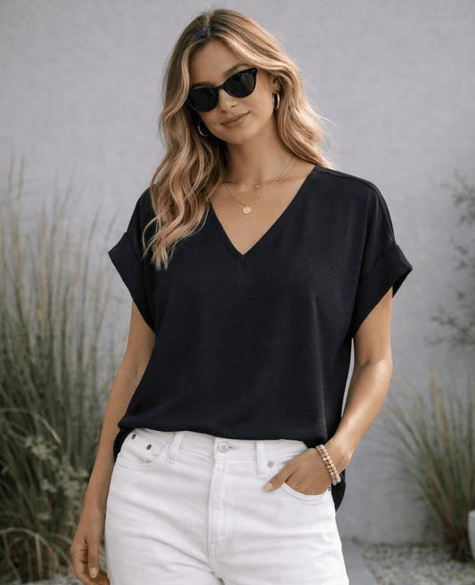 Woman wearing a black top and white pants with sunglasses outdoors.