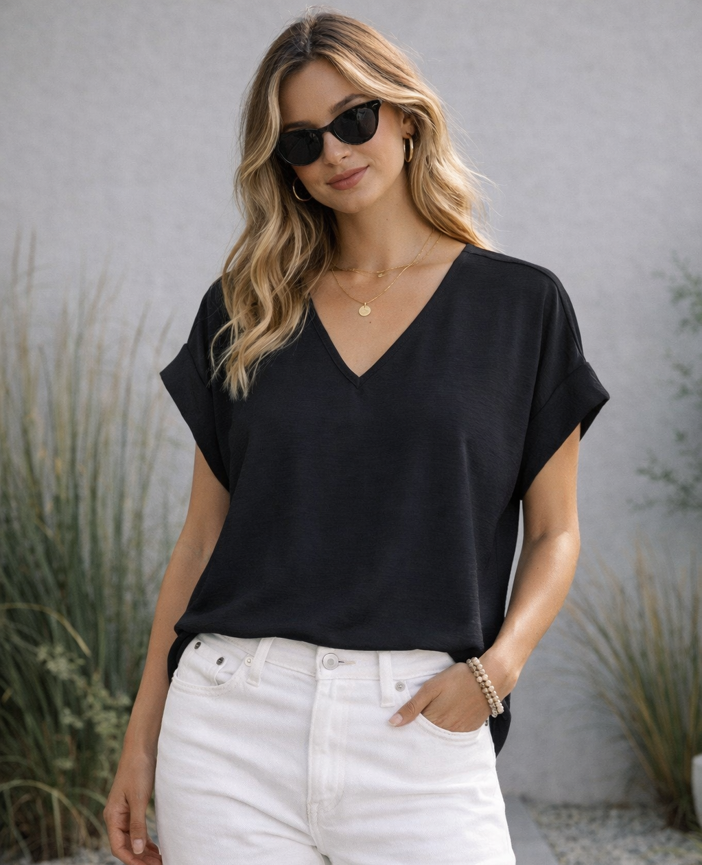 Woman wearing a black top and white pants with sunglasses outdoors.