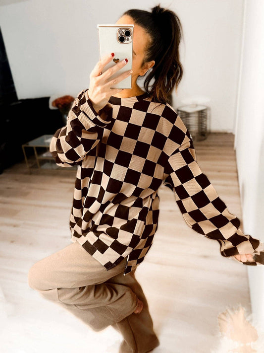 Person wearing a black and beige checkered shirt in a room with white walls and wooden floor.