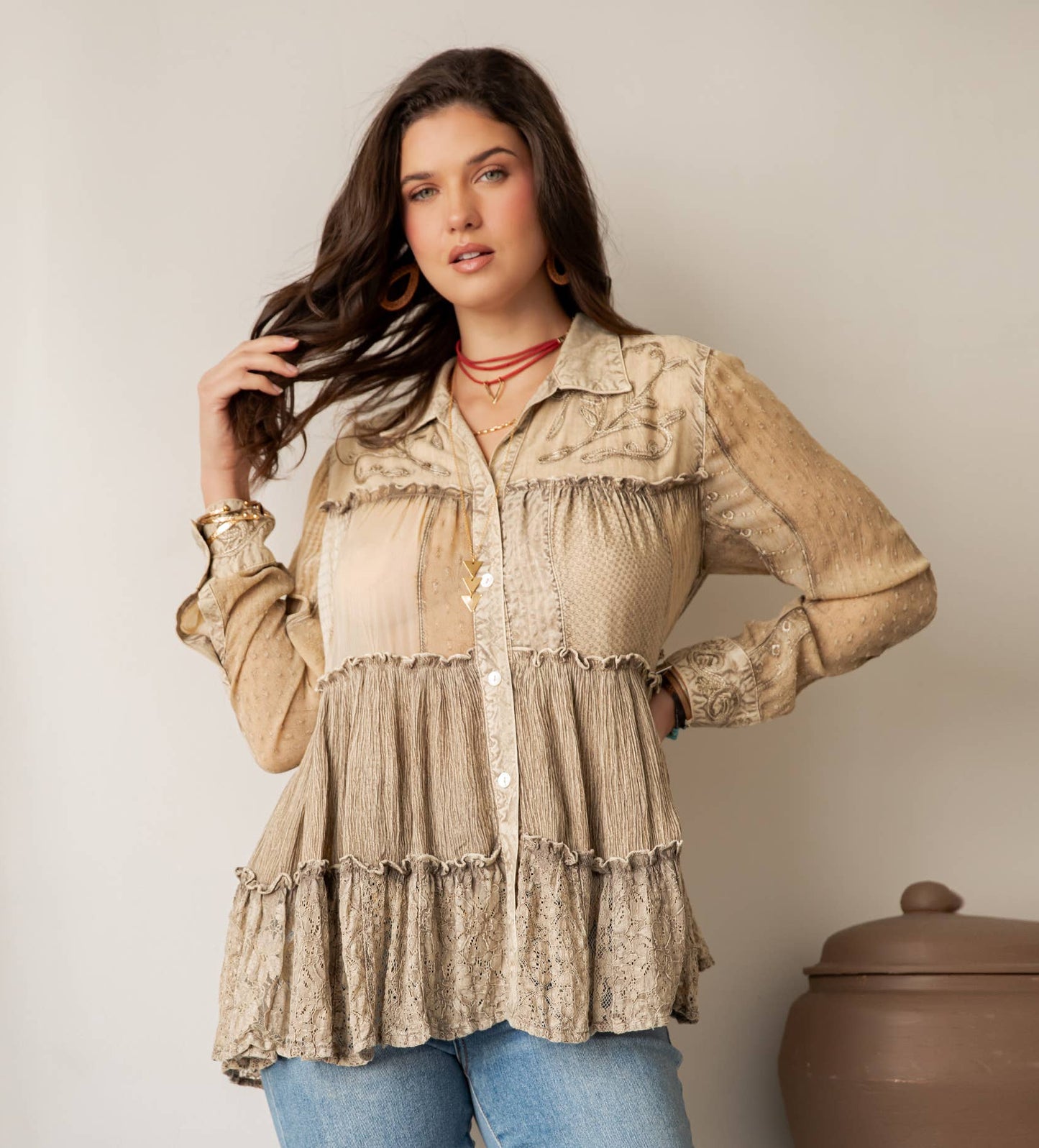 Woman wearing a beige lace blouse and blue jeans against a neutral background