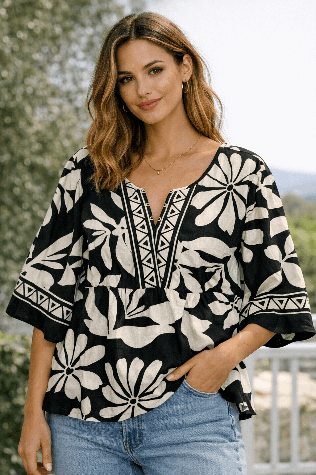 Woman wearing a black and white patterned blouse with blue jeans outdoors.