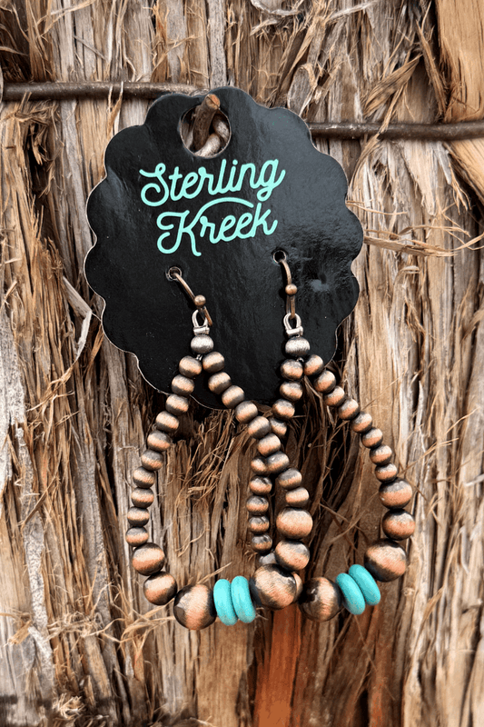 Copper and turquoise beaded earrings on a wooden background with 'Sterling Kreek' branding.