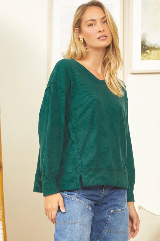 Woman wearing a green sweater and blue jeans indoors.