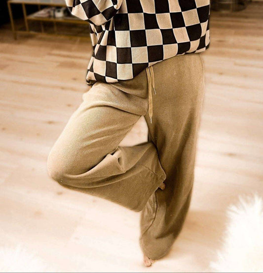 Person wearing a checkered shirt and beige pants on a wooden floor.