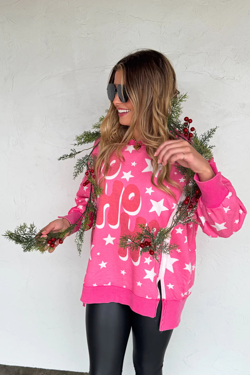 Woman wearing a pink Christmas-themed sweater with white stars and text that says HoHoHo