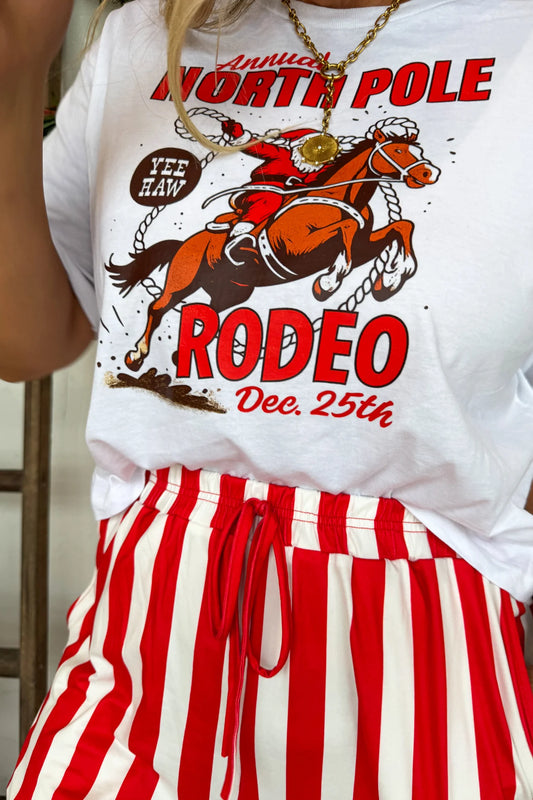 Person wearing a white t-shirt with a 'North Pole Rodeo' graphic and red and white striped pants.