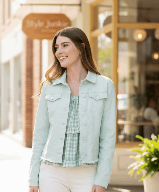 Woman in a light green jacket standing on a city street with a store in the background