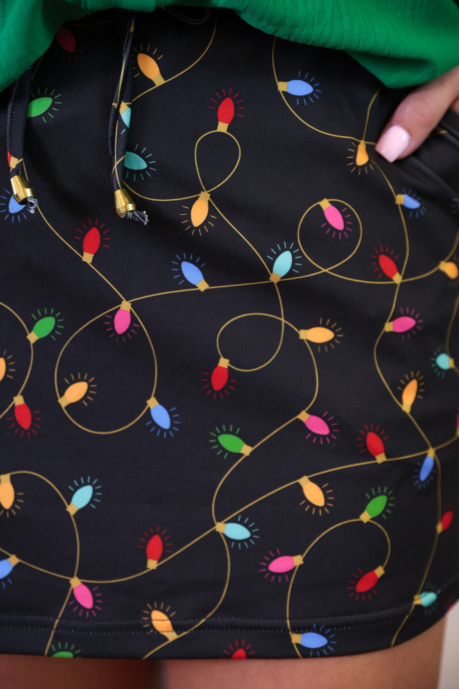 Black shorts with colorful Christmas light pattern worn by a person in a green sweater.